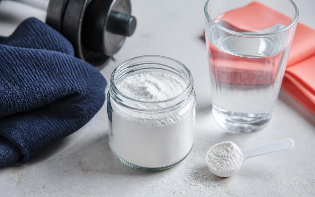 Creatine monohydrate powder beside water and training equipment